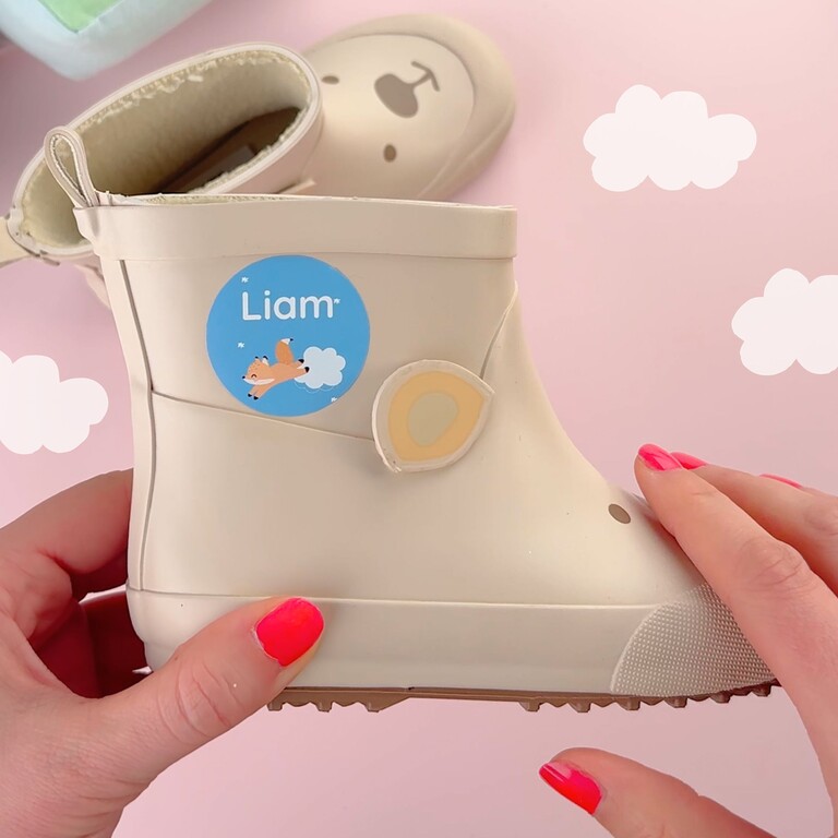 Grande étiquette nominative bleue avec design renard et le prénom Liam, posée sur une botte beige