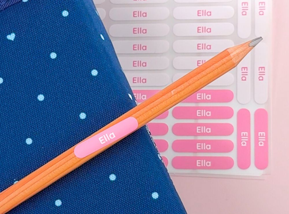 Les types d’étiquettes nominatives expliqués – laquelle devrais-tu choisir? 4 Étiquette nominative rose avec le prénom ella sur un crayon, à côté d’une planche de stickers assortie
