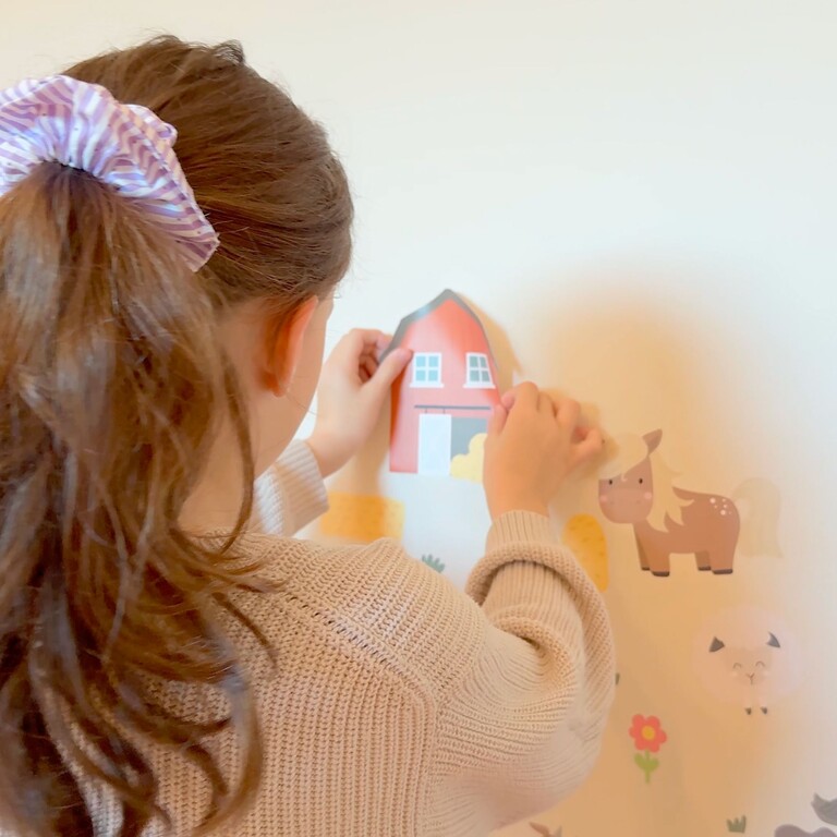 Fille collant des stickers muraux animaux de la ferme sur le mur