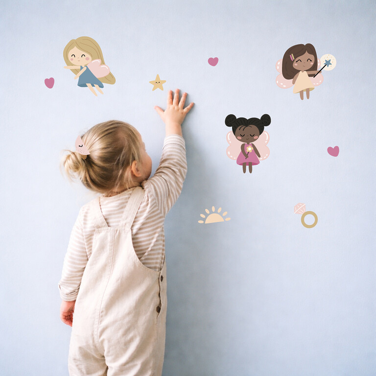 Fille collant des stickers muraux fées sur le mur